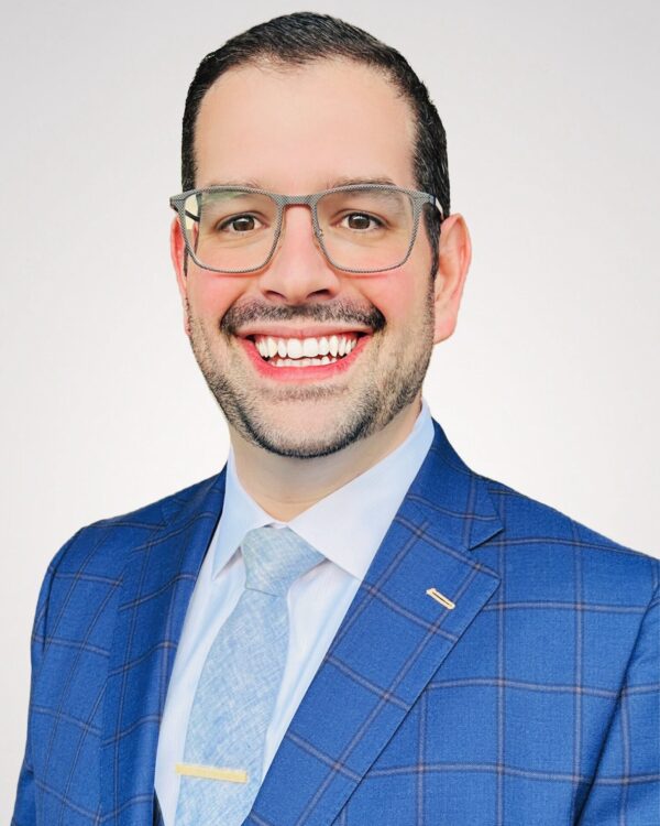 man in light blue suite with glasses smiling