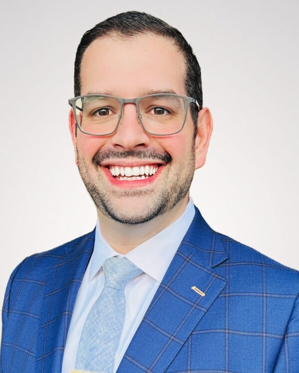 man in light blue suite with glasses smiling