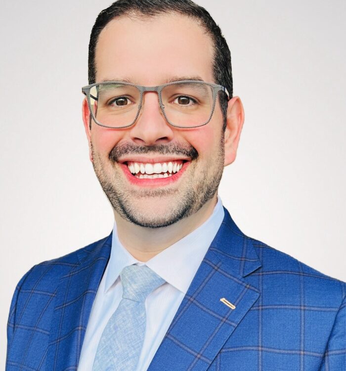 man in light blue suite with glasses smiling